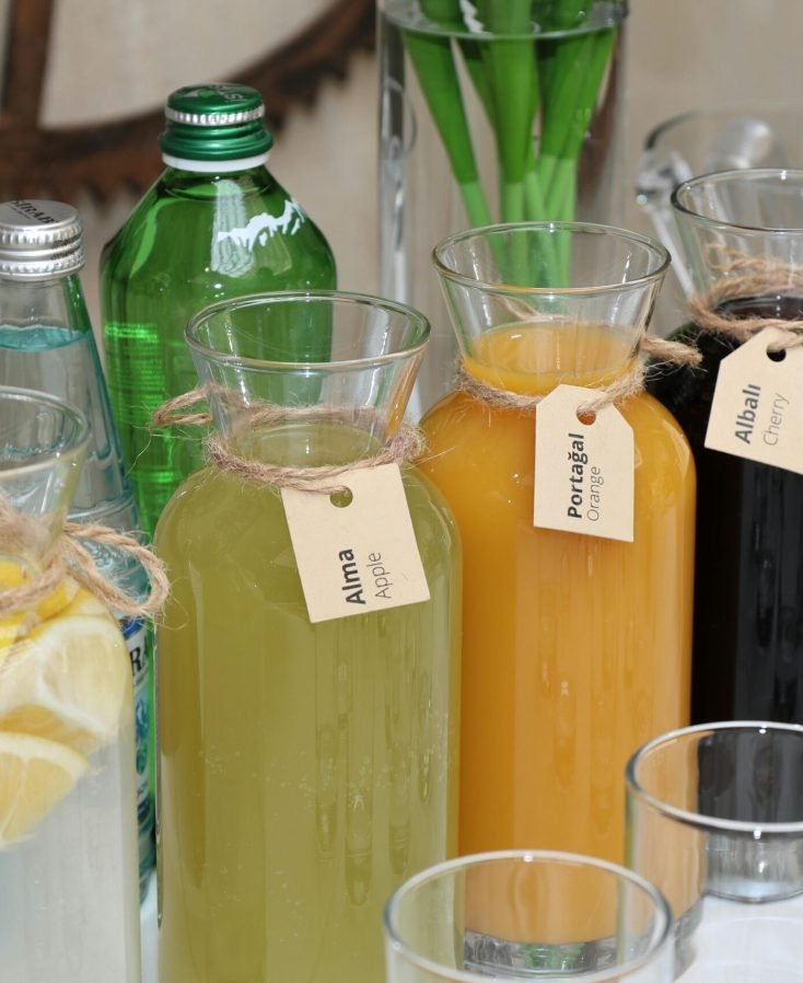 Vibrant assortment of fresh juices in labeled glass bottles with water bottles and glasses arranged outside on a table.