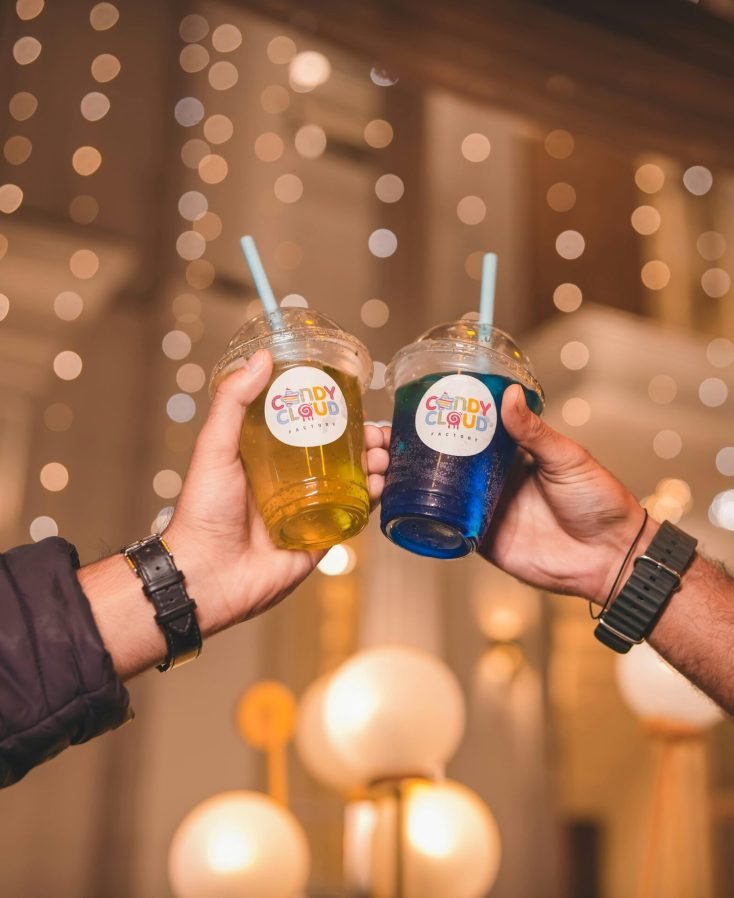 Two people clinking colorful drinks with straws, creating a festive mood.