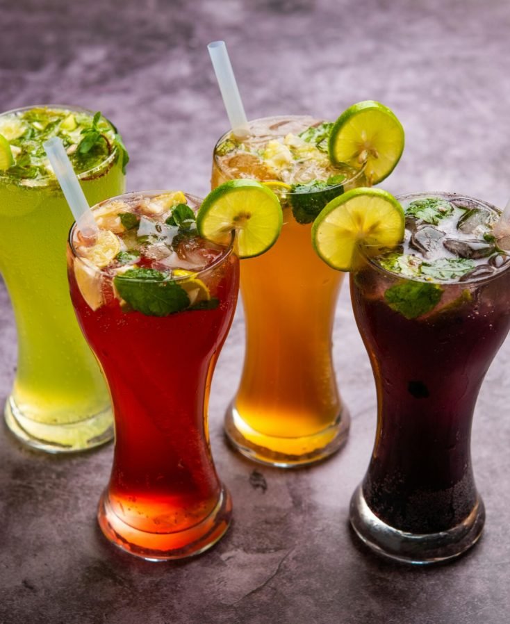 Four vibrant lemon and mint garnished drinks served in tall glasses with straws.
